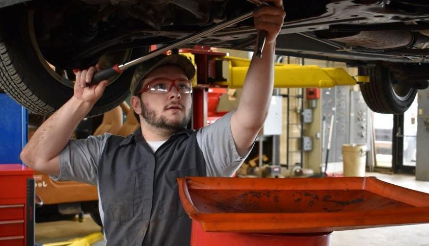 student in auto shop working on diesel engine while car is on a lift